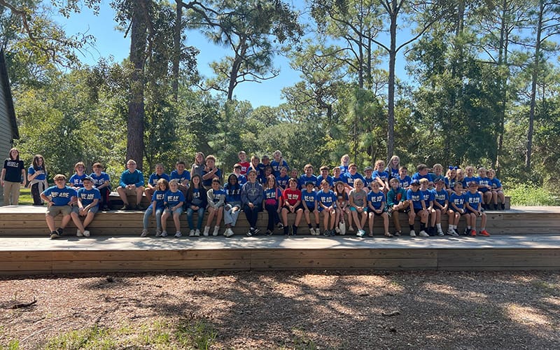 Group of students posing for a photo outdoors on wooden bleachers