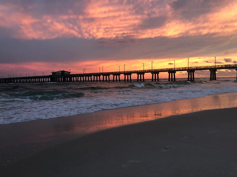 Sunset over the ocean with colorful skies behind a pier