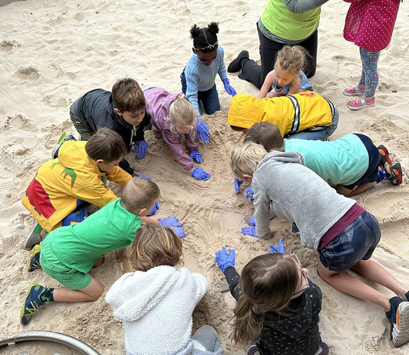Children wearing gloves digging and playing together in a sandbox
