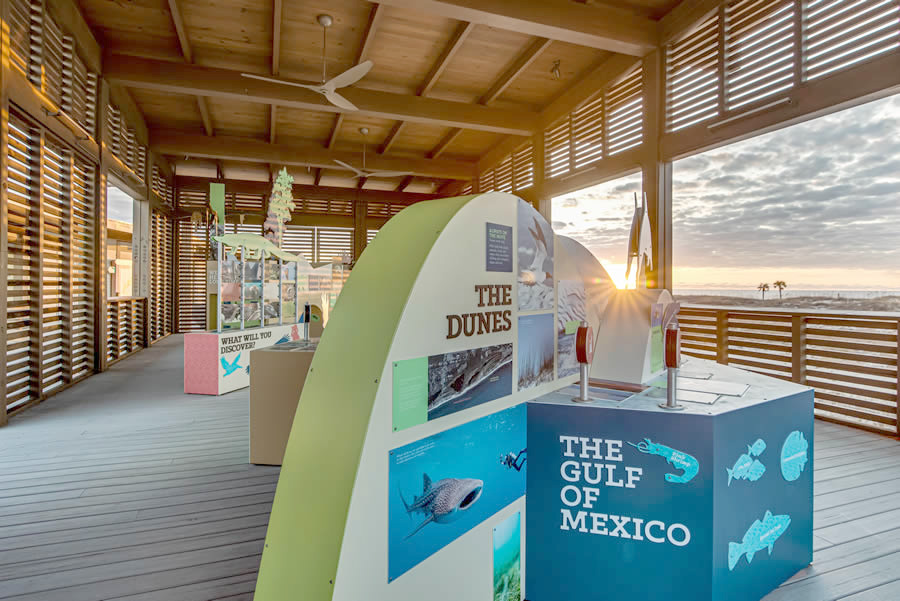 Sunset view behind an educational exhibit on coastal environments in an open-air wooden pavilion