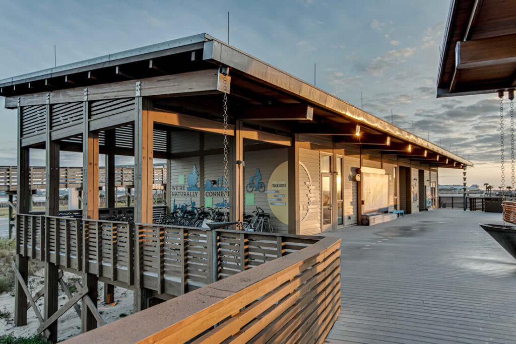 Modern beachfront community center with bicycle station and outdoor seating area at sunset