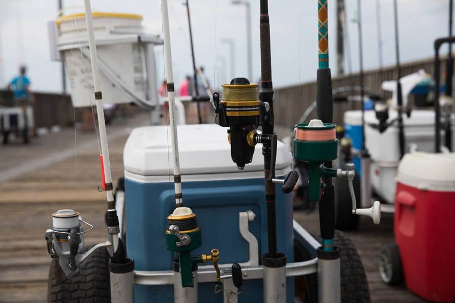 Fishing rods mounted on a cart at a pier with people in the background