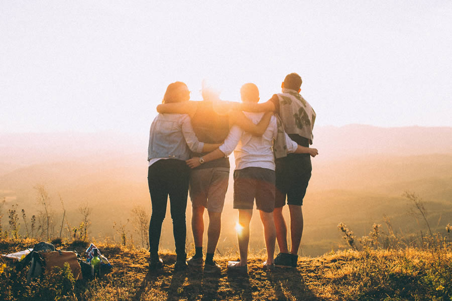 Group of friends embracing at sunset on a hill, emphasizing friendship and nature