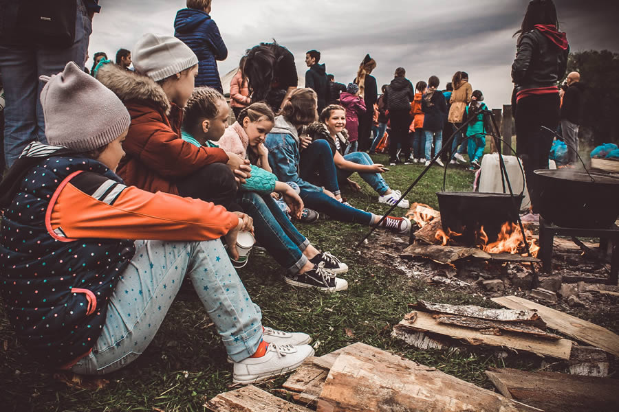 Group of people gathered around a campfire in an outdoor setting, engaging socially