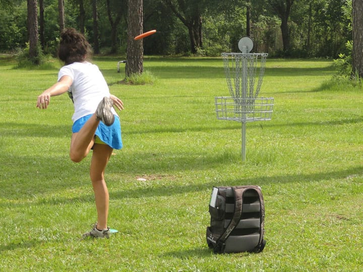 Person playing disc golf aiming at a metal basket in a park